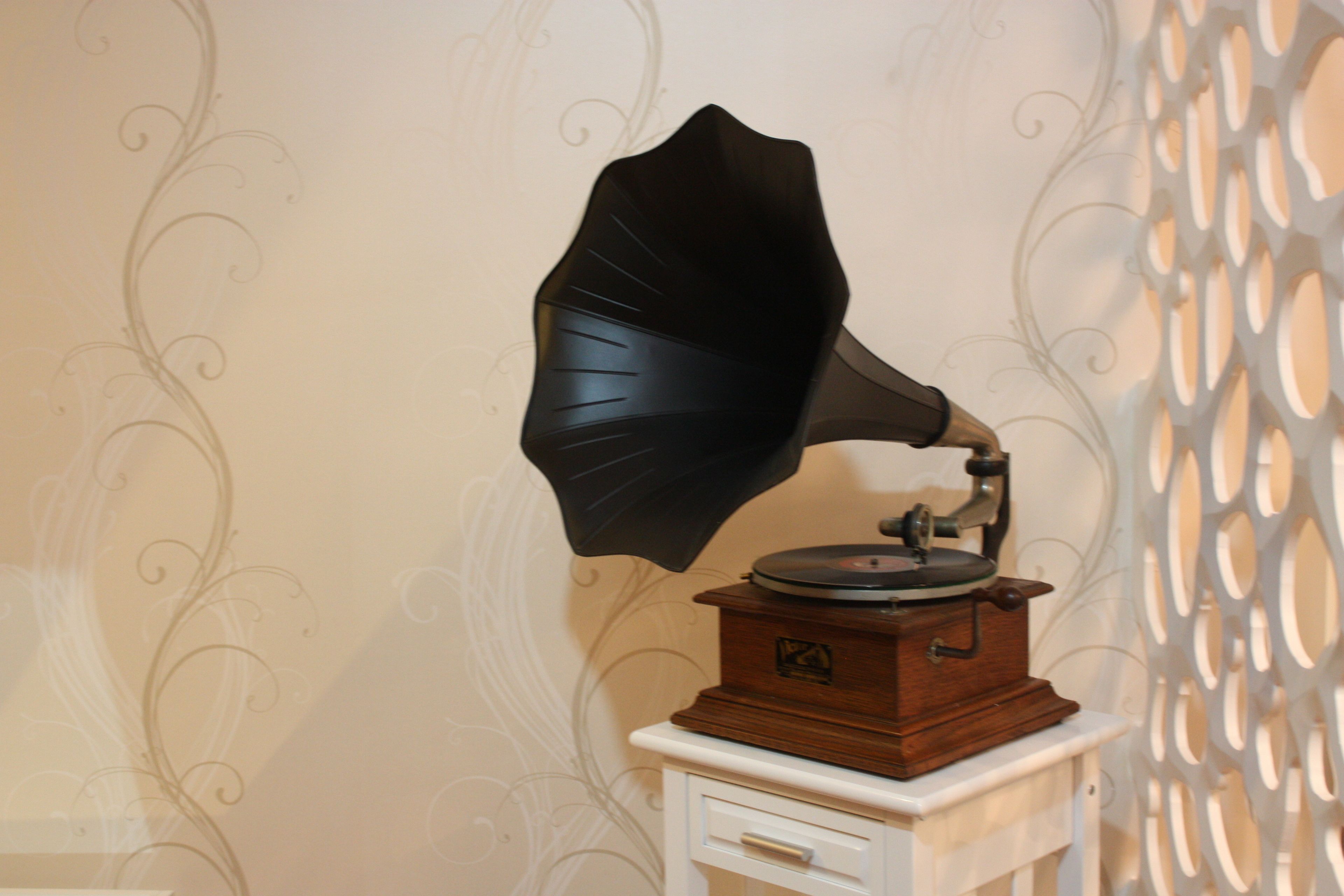 A vintage gramophone on a small white table against a wall with decorative wallpaper.