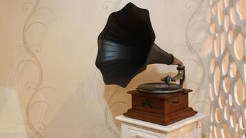 A vintage gramophone on a small white table against a wall with decorative wallpaper.