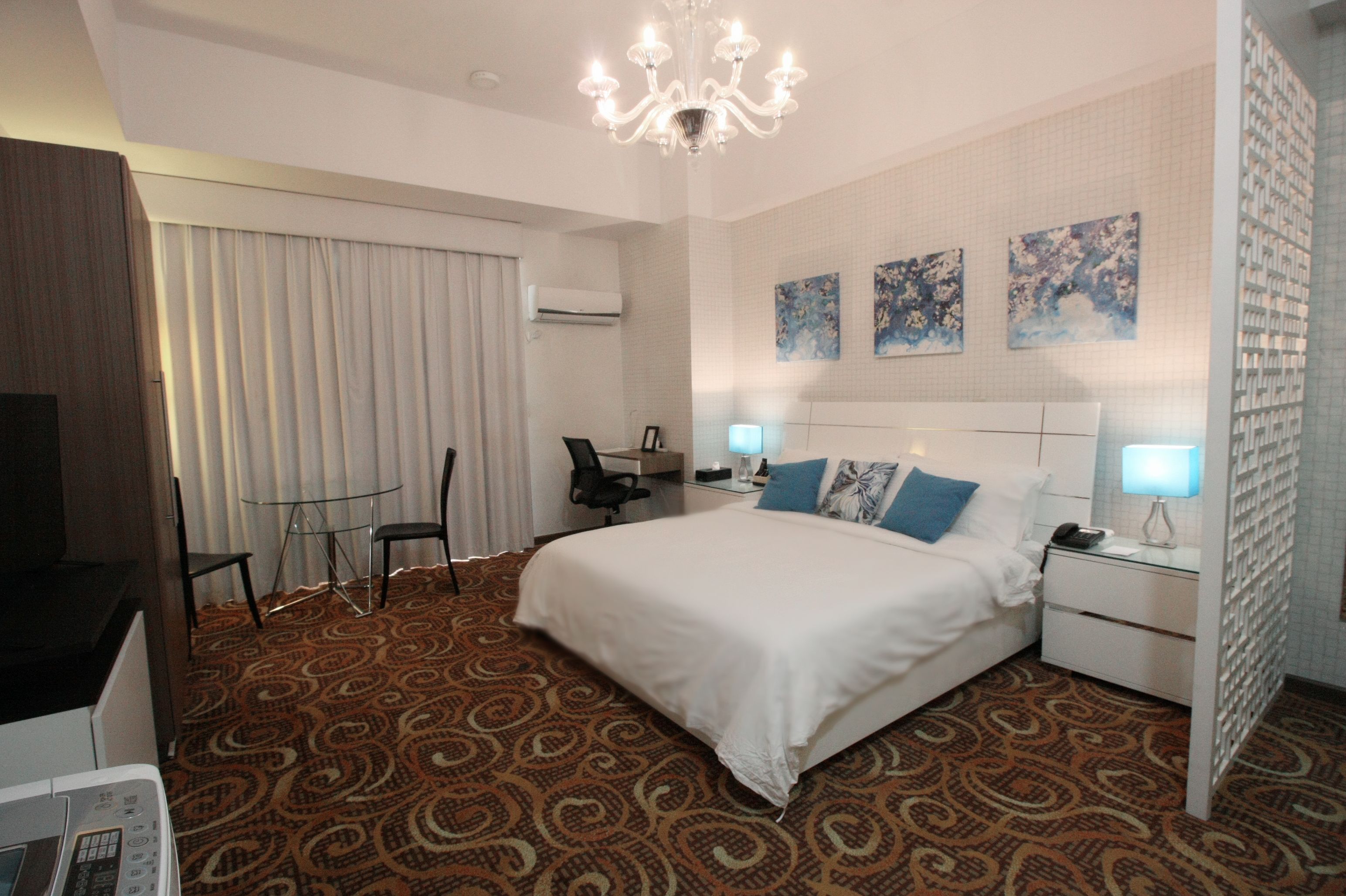 Une chambre d’hôtel avec un grand lit, un bureau avec une chaise, une télévision et un lustre.