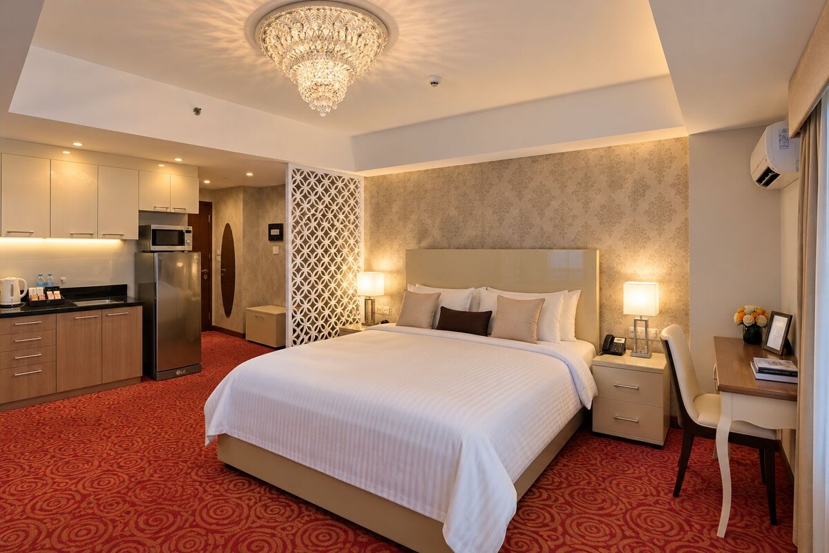 Habitació d'hotel amb un llit gran, un escriptori, una cadira, una cuineta i un penjador.