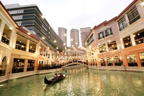 A gondola ride through a canal flanked by high-rise buildings with balconies and outdoor seating areas. - MaxStays Max Pavilion at The Venice Residences (Taguig)