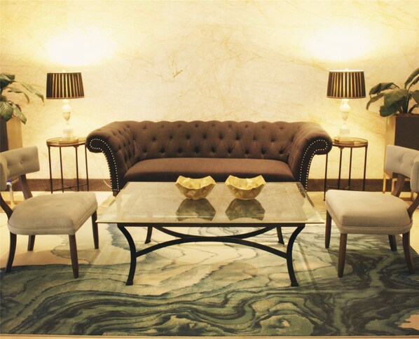 Un canapé marron à motifs capitonnés, accompagné de deux fauteuils assortis, une table basse en verre et deux petites tables d’appoint avec des lampes.