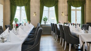 A formal dining room with long tables set for a meal, large windows with green curtains, and a radiator between the tables. - Stiftsgården Södra Hoka (Asarum)