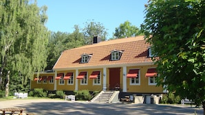 A yellow building with a red roof, red awnings, and a staircase leading to the entrance. - Stiftsgården Södra Hoka (Asarum)