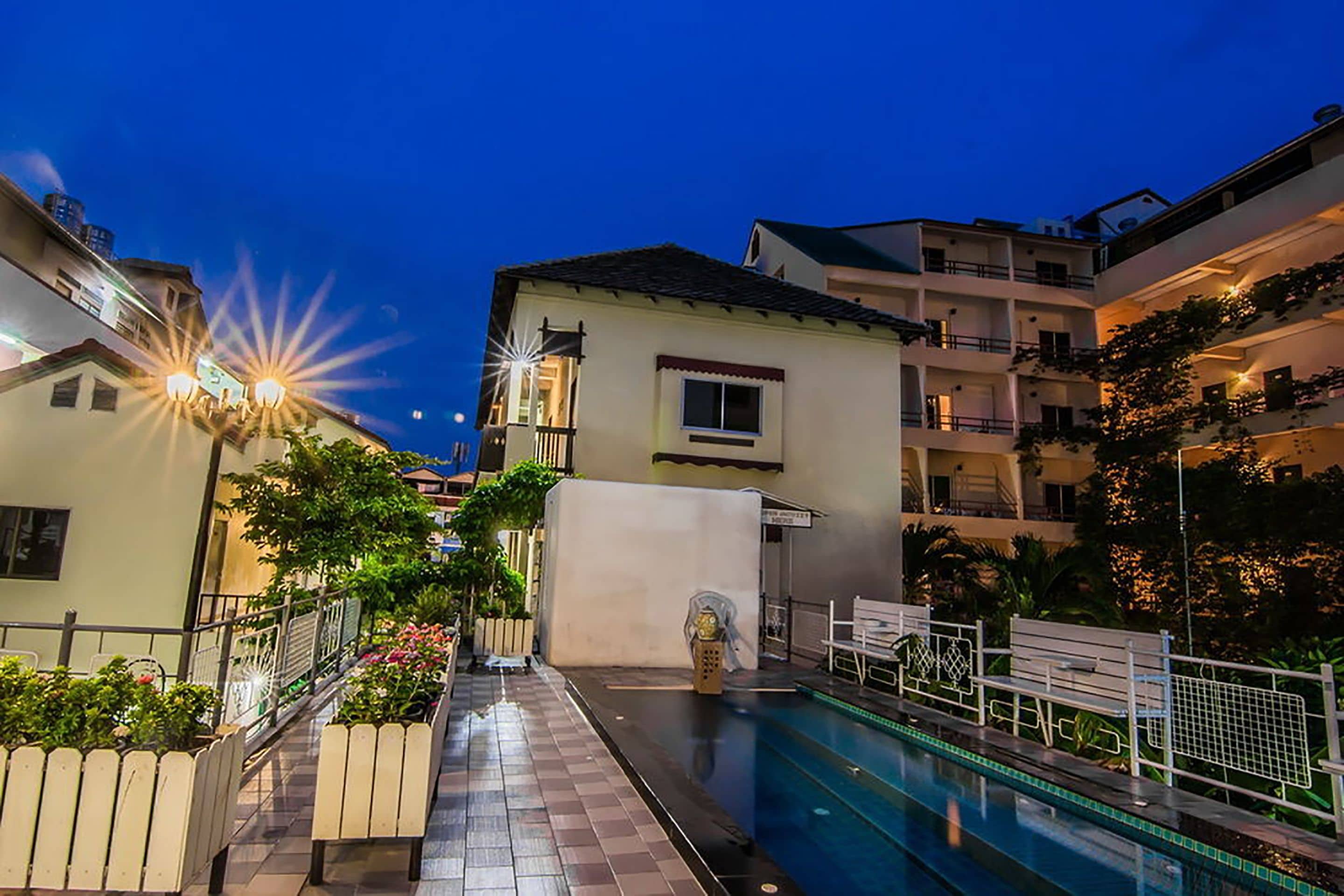 A pool area with a tiled walkway, benches, and a building with balconies.