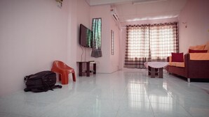 Una sala de estar con sofá, televisor, sillón rojo, una mesita y una ventana con cortinas.