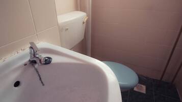 Um banheiro com pia branca, vaso sanitário azul e piso revestido de azulejos.