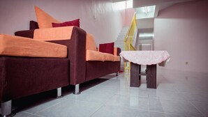 Una sala de estar con un sofá, una mesita con mantel de encaje y una escalera al fondo.