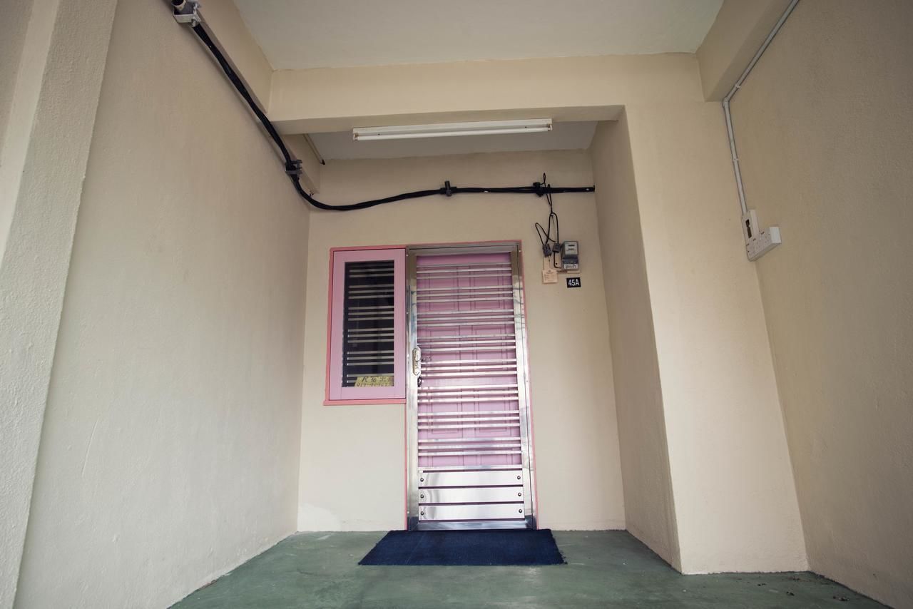 Un couloir étroit avec une porte, une fenêtre munie de stores, un luminaire fluorescent et une prise de courant sur le mur.