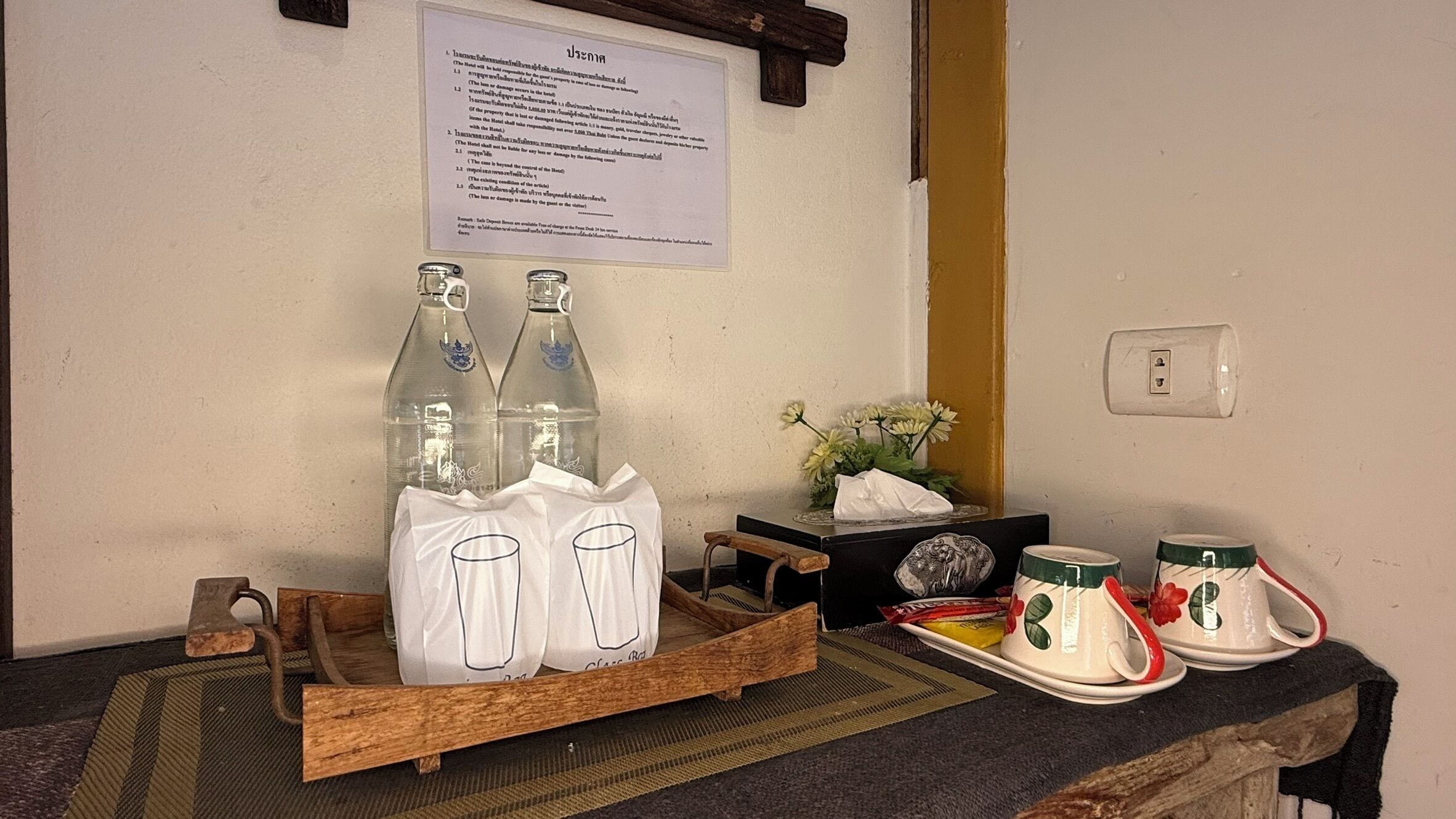A room with a wooden table displaying bottles, a tray with glasses, and a sign on the wall.