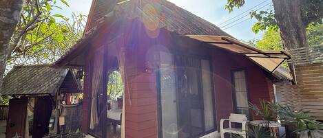 A rustic house with a red exterior, large glass windows, and a small porch area with a chair and table.