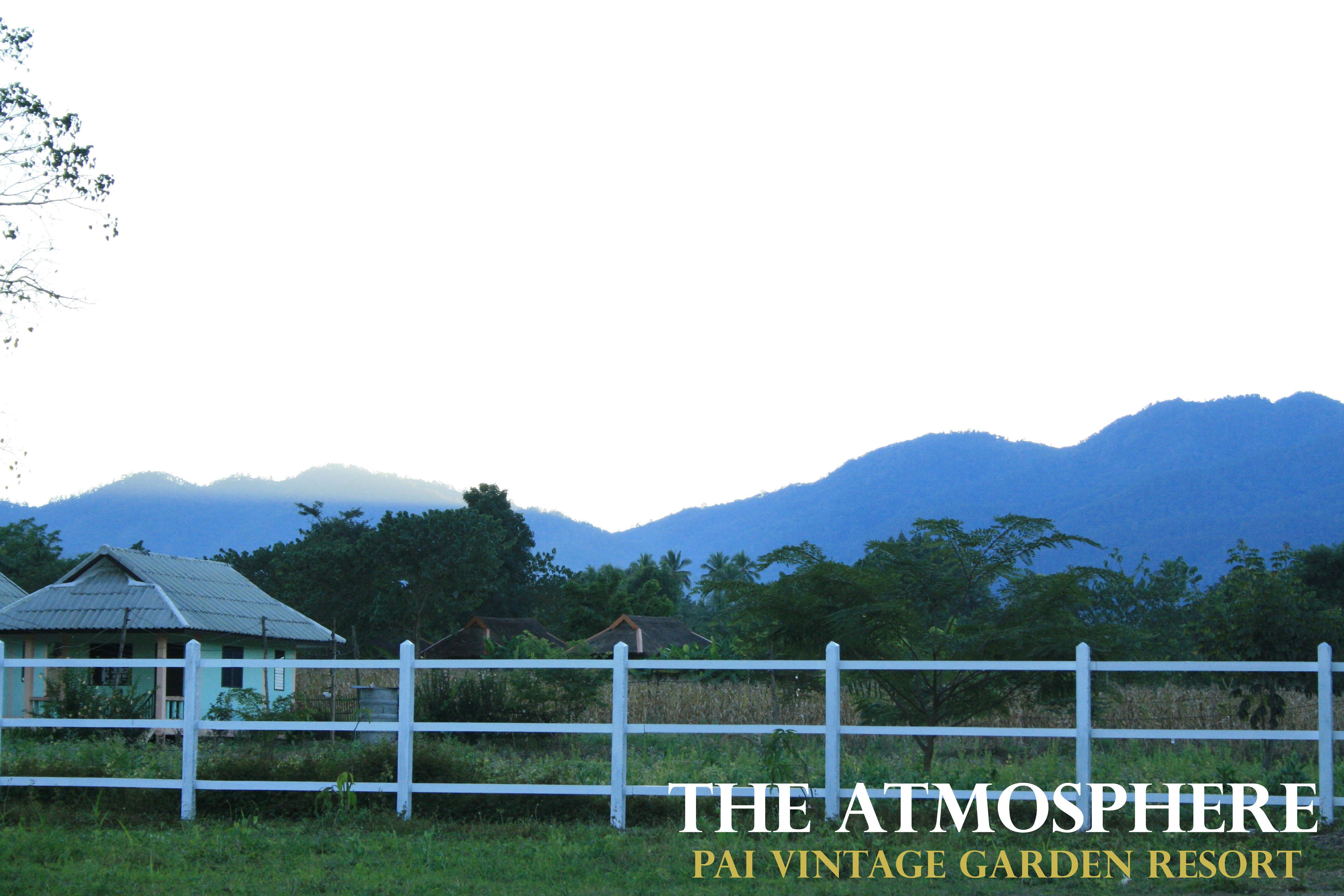 A rustic house with a white fence in a lush green landscape with mountains in the background.