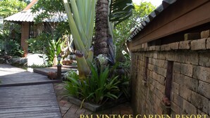 Un jardin avec une terrasse en bois, un palmier et un mur en briques.