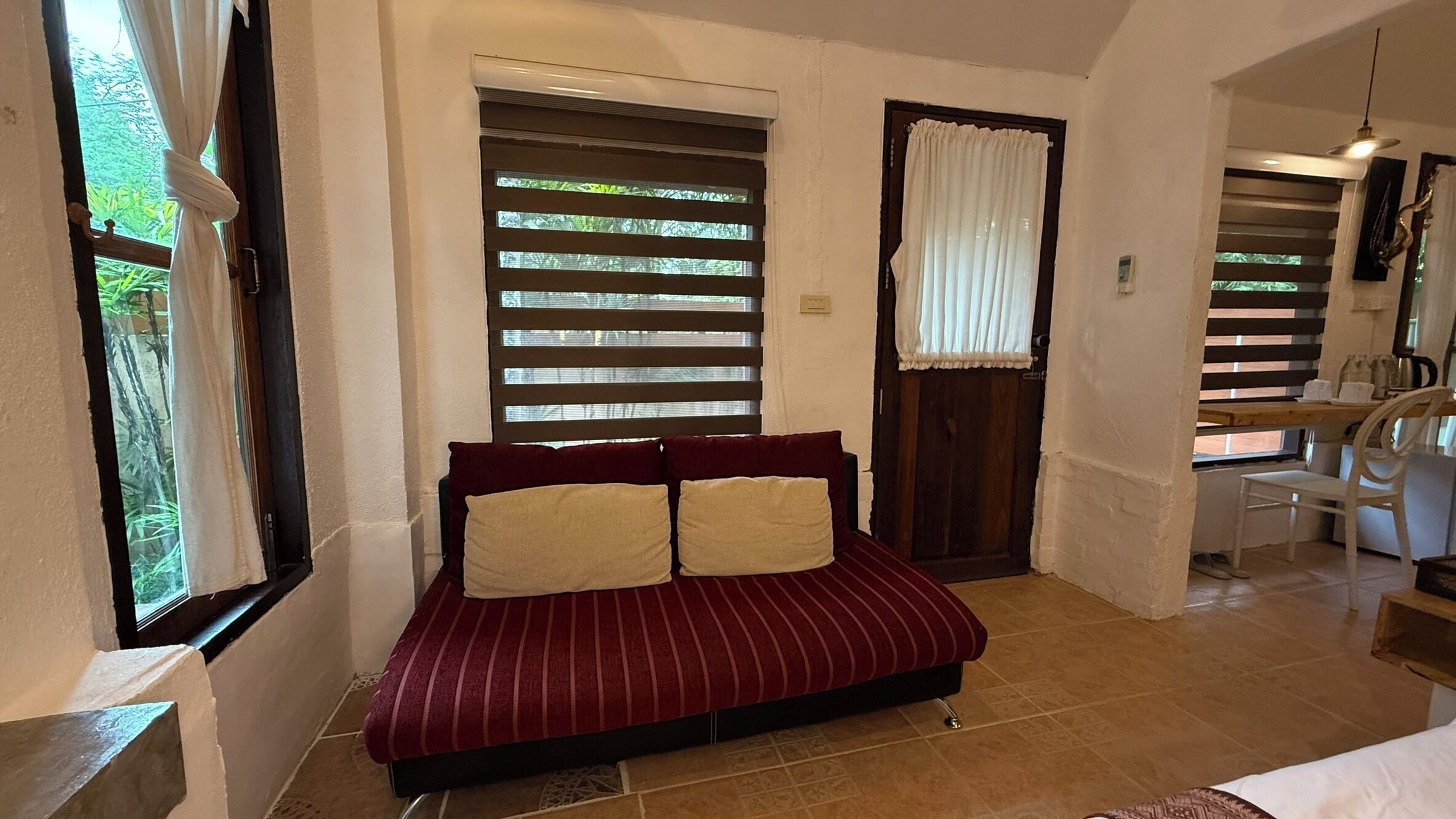 A room with a bed, a window with blinds, a door, and a small table with chairs.