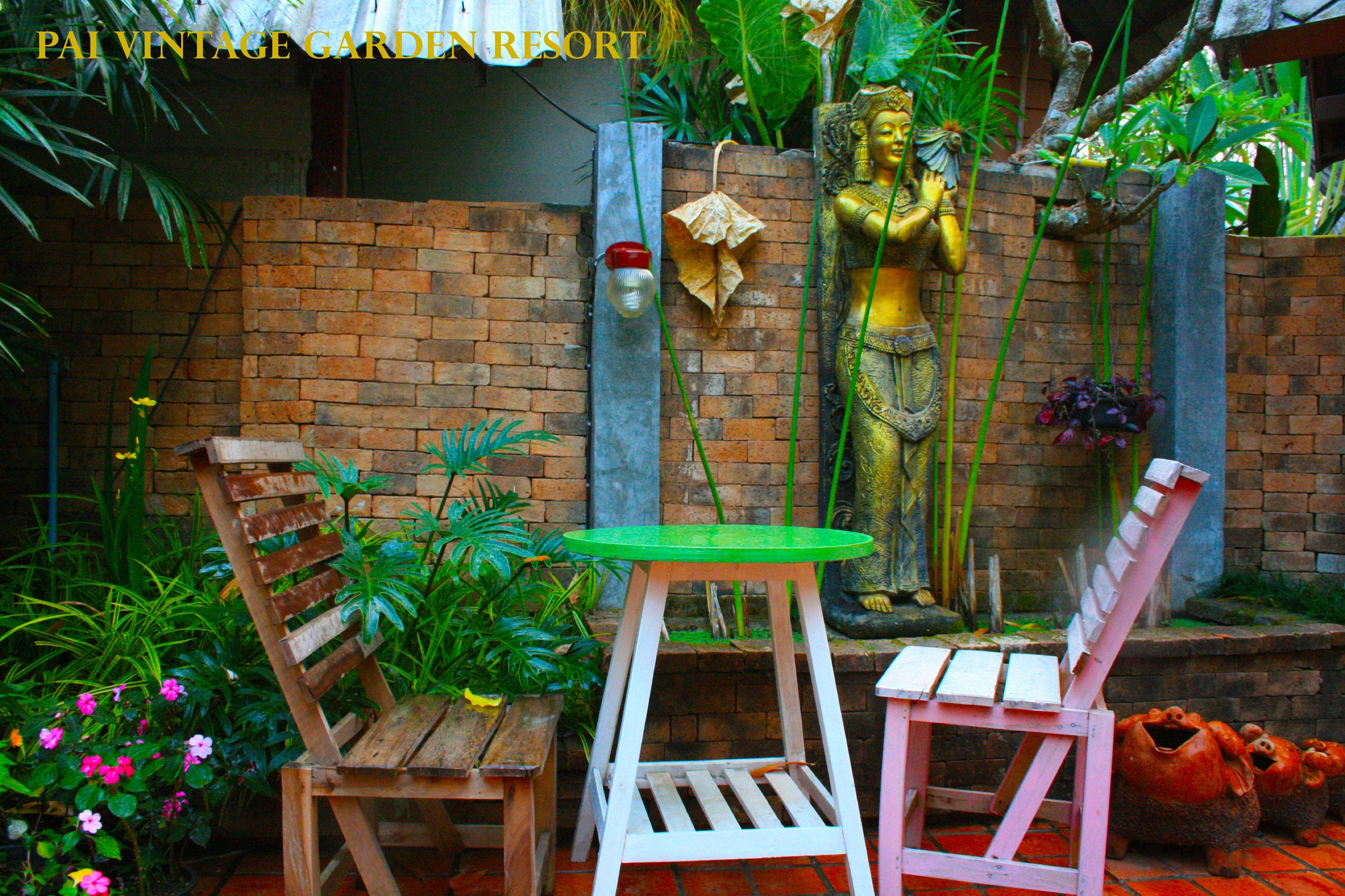 Un jardín con muro de ladrillo, una estatua y mobiliario de madera.