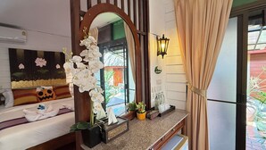 Une chambre d’hôtel avec un lit, un grand miroir, une fenêtre avec des rideaux, une petite lampe de chevet et une petite table sur laquelle se trouvent une plante et des bouteilles.