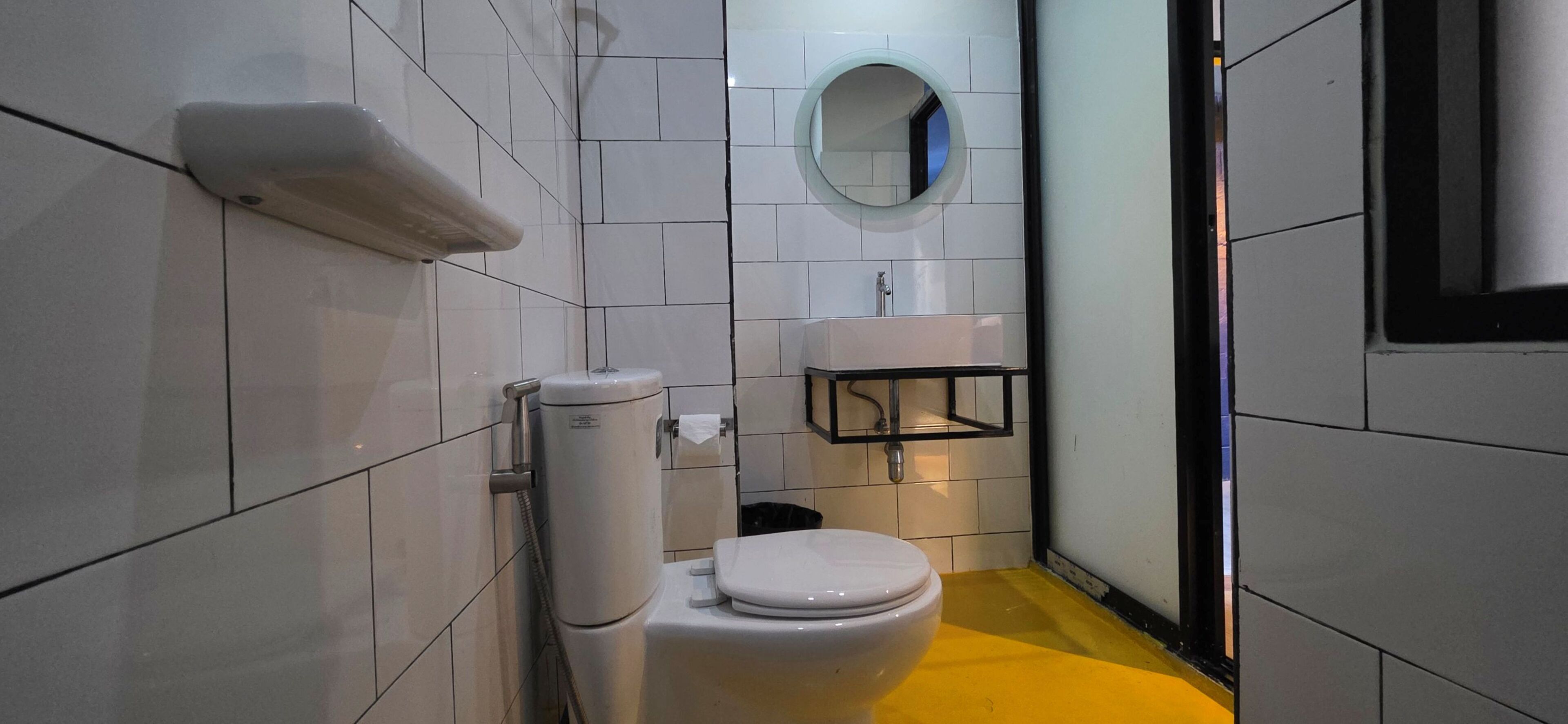 A small, modern bathroom with white tiles, a toilet, a sink, and a mirror.