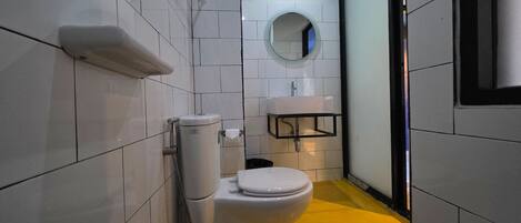 A small, modern bathroom with white tiles, a toilet, a sink, and a mirror.