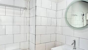 A bathroom with white tiled walls, a yellow floor, a white toilet, a white sink with a black frame, and a round mirror.