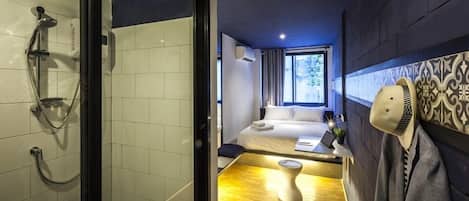 A hotel room with a shower, a bed, a bedside table with a laptop, and a window with curtains.