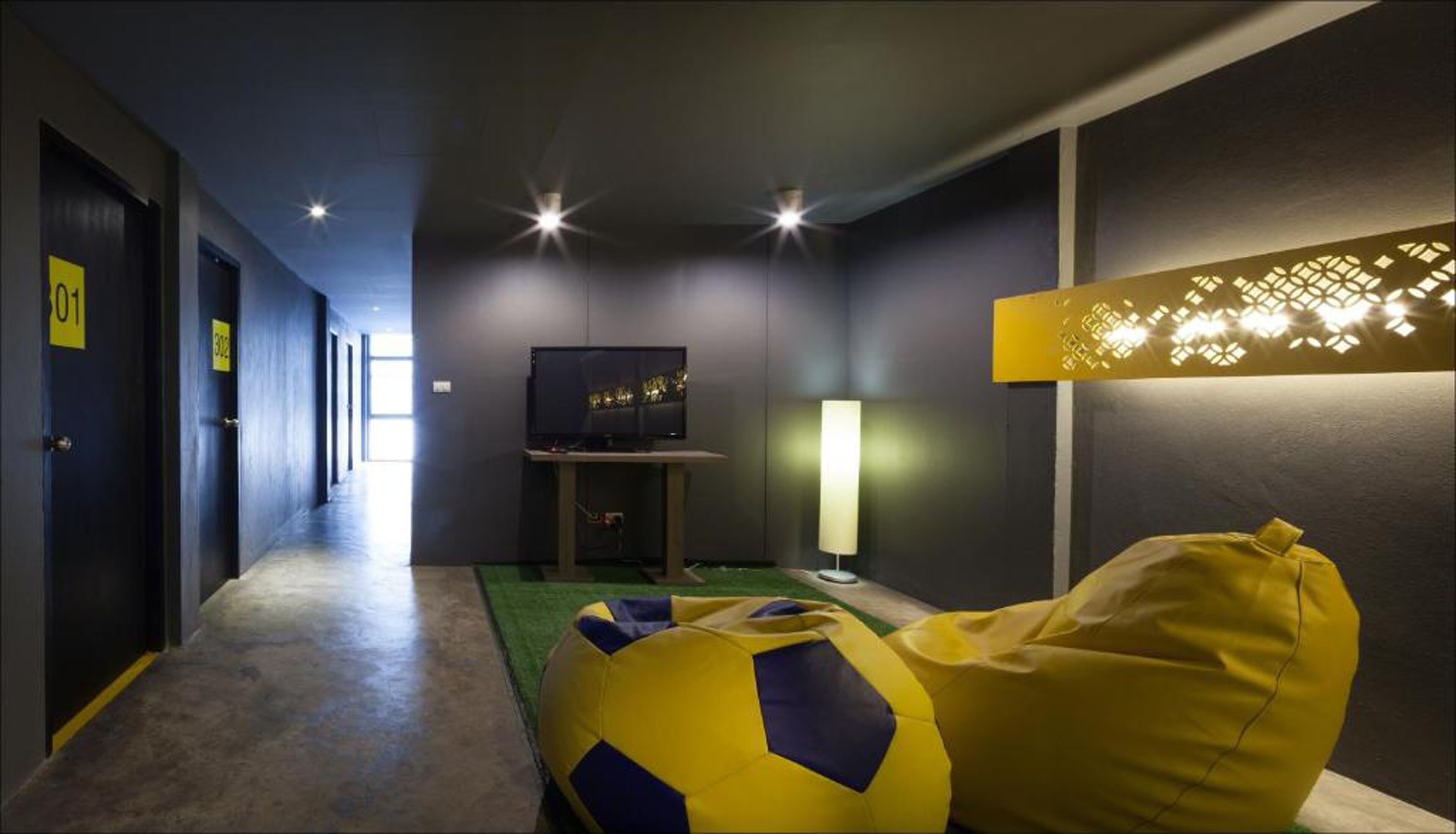 Habitación de hotel con pasillo, televisor sobre un mueble, lámpara y sillón de peluche.
