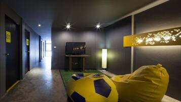 Habitación de hotel con pasillo, televisor sobre un mueble, lámpara y sillón de peluche.