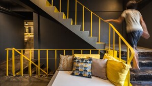 Una escalera con barandillas amarillas que lleva a un rellano con una cama y almohadas.