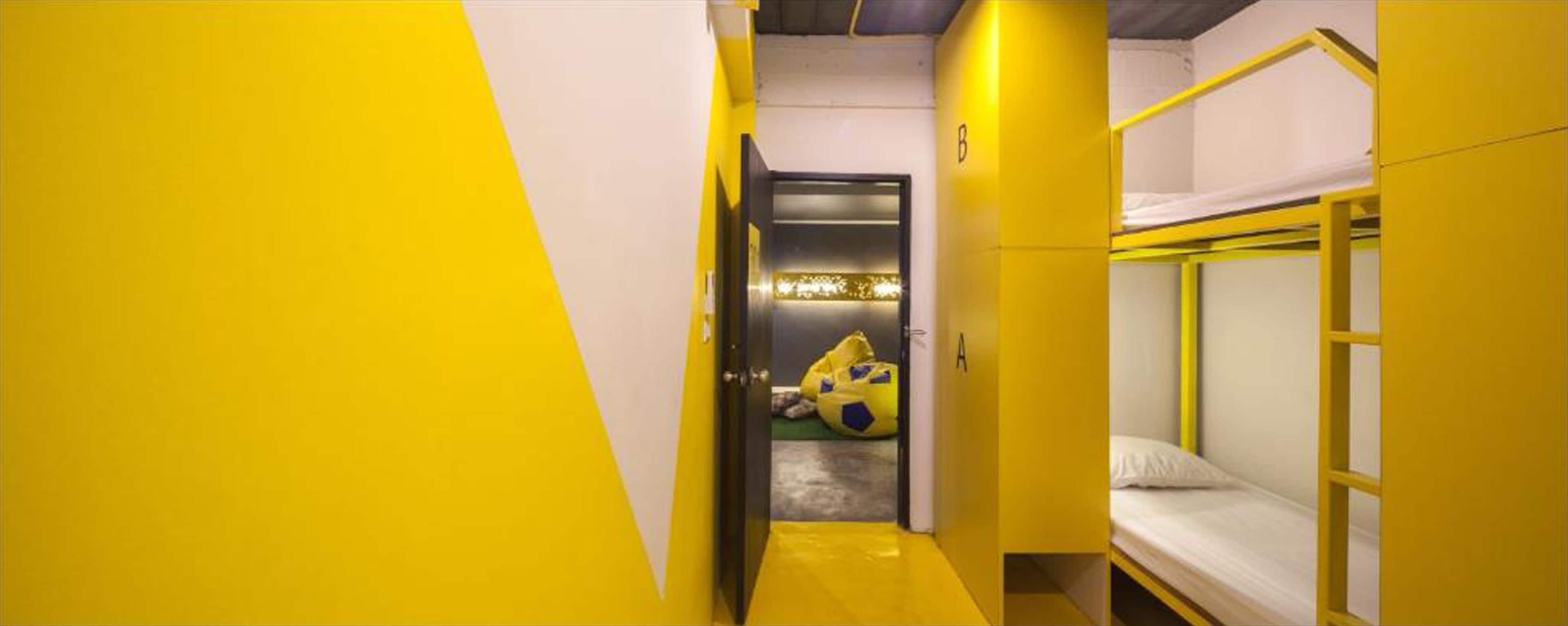 A narrow hallway with yellow walls leading to a room with bunk beds and a door.