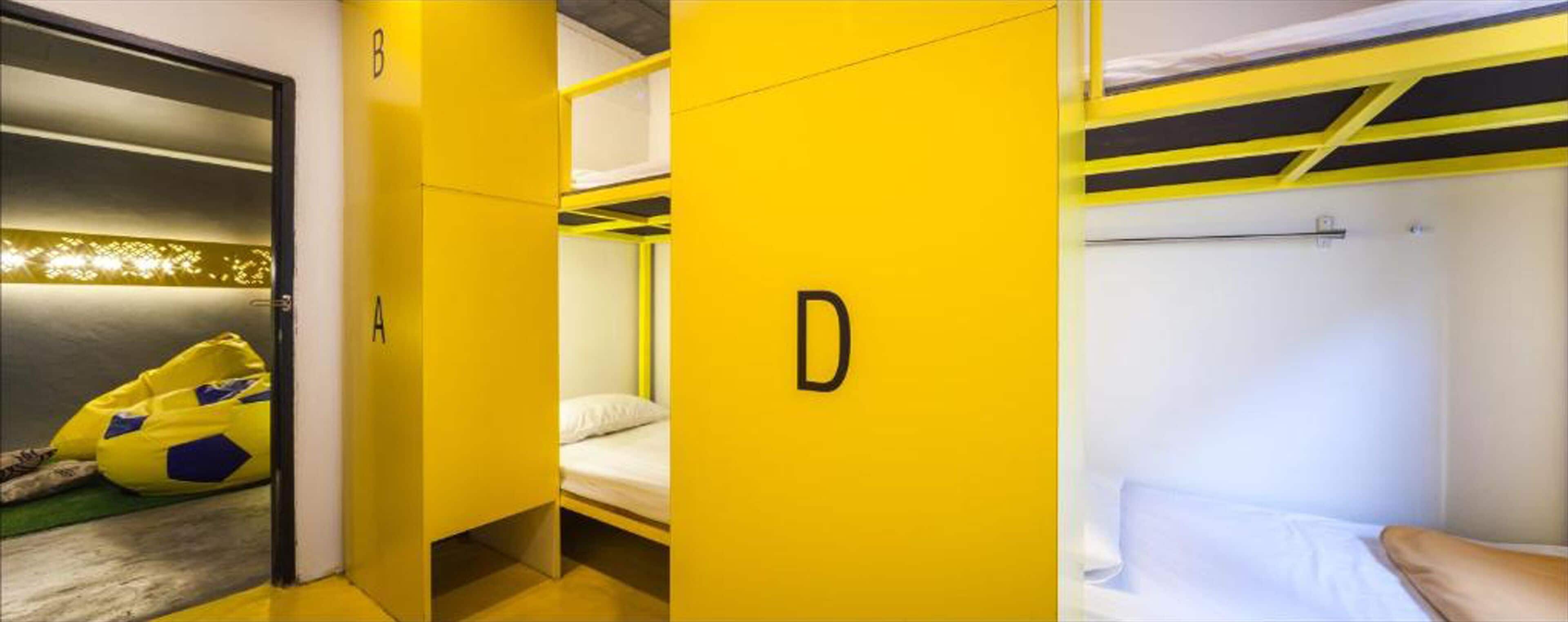 Um dormitório com beliches, um guarda-roupa amarelo e uma cama com colchão branco.