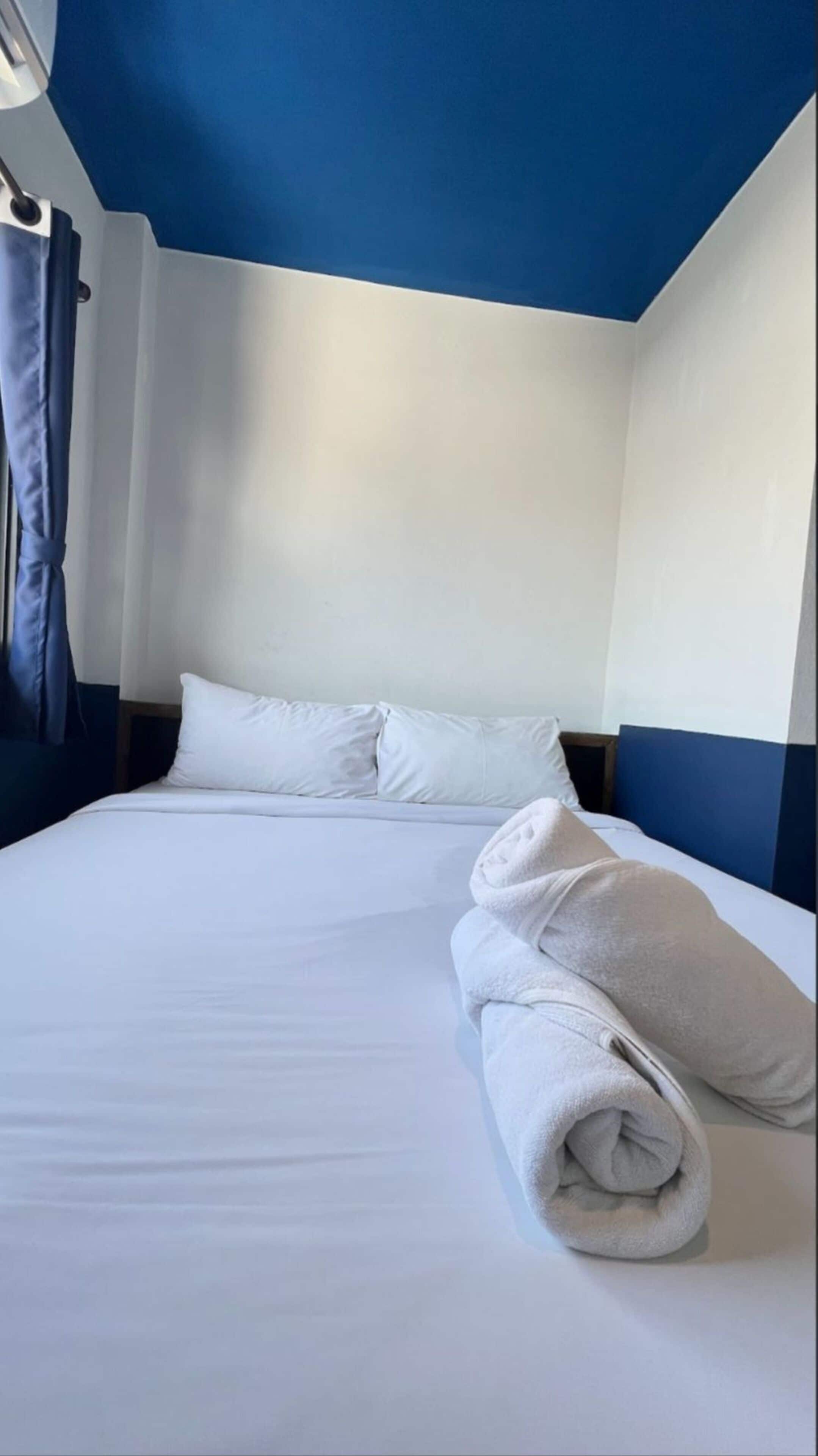 A hotel room with a bed, pillows, and a rolled towel.