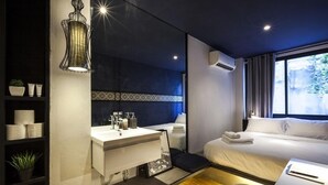 Una habitación de hotel moderna con un espejo grande, una mesita de noche, una cama y una ventana con cortinas.