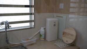 A bathroom with a sink, a white water dispenser, a bottle of liquid soap, and a wooden cutting board on a rack. - Holidayhome 188 Taman Sejati Suria (Sitiawan)