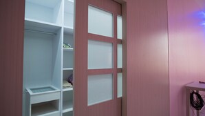 Ein begehbarer Kleiderschrank mit mehreren Regalen und einer Kleiderstange, ein kleiner Tisch mit Kabel sowie eine rosa Wand.