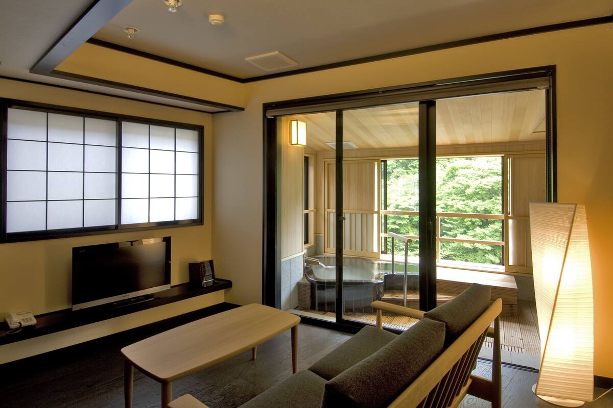 A modern room with a sofa, a table, a TV, and a sliding glass door leading to a balcony with a hot tub.