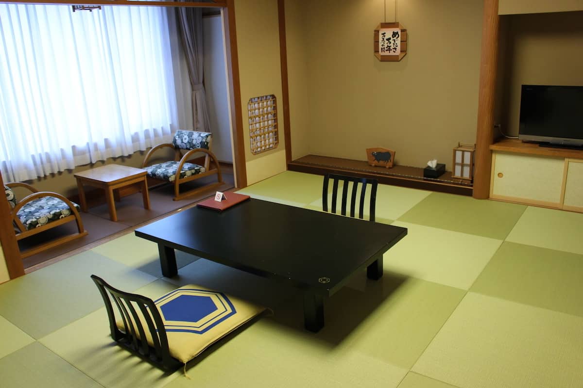 A traditional Japanese-style room with tatami flooring, a low table, and a television on a cabinet.