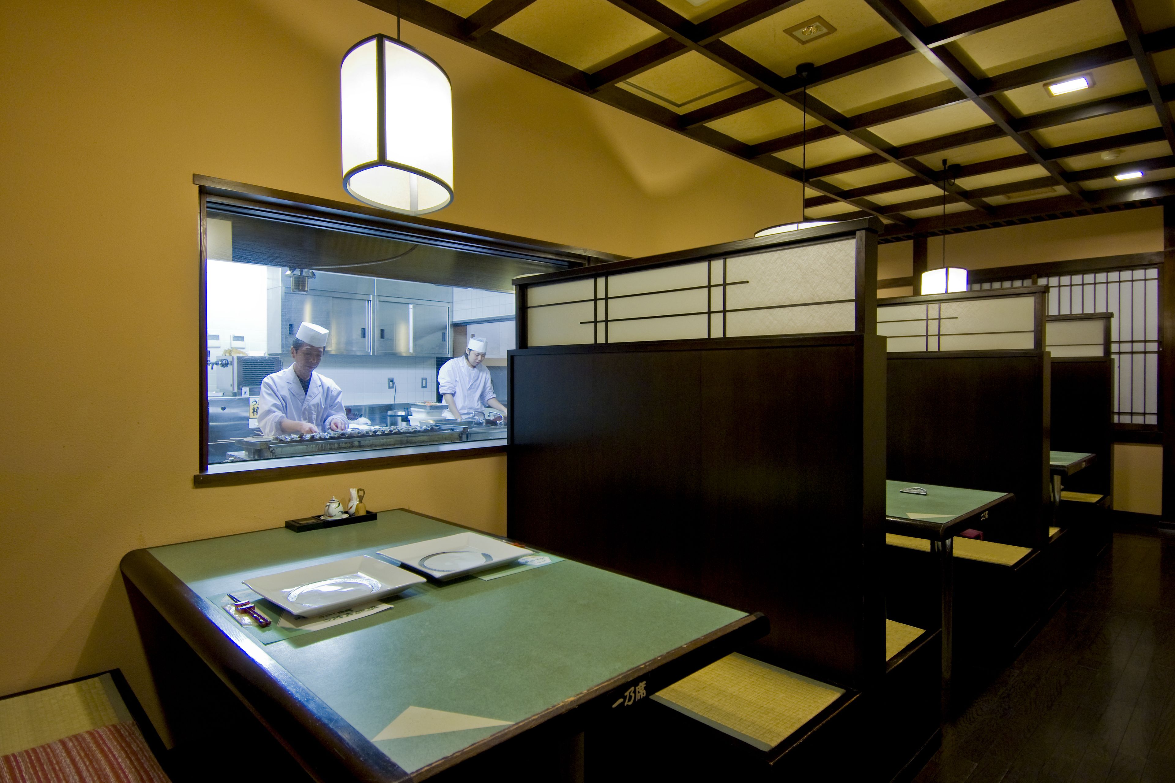 A restaurant with a traditional Japanese interior, featuring tatami mats, low tables, and a view of the kitchen area.