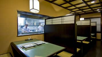 A restaurant with a traditional Japanese interior, featuring tatami mats, low tables, and a view of the kitchen area.