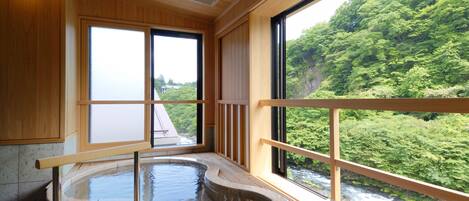 A hot spring bath with wooden railings and a view of a forested area.