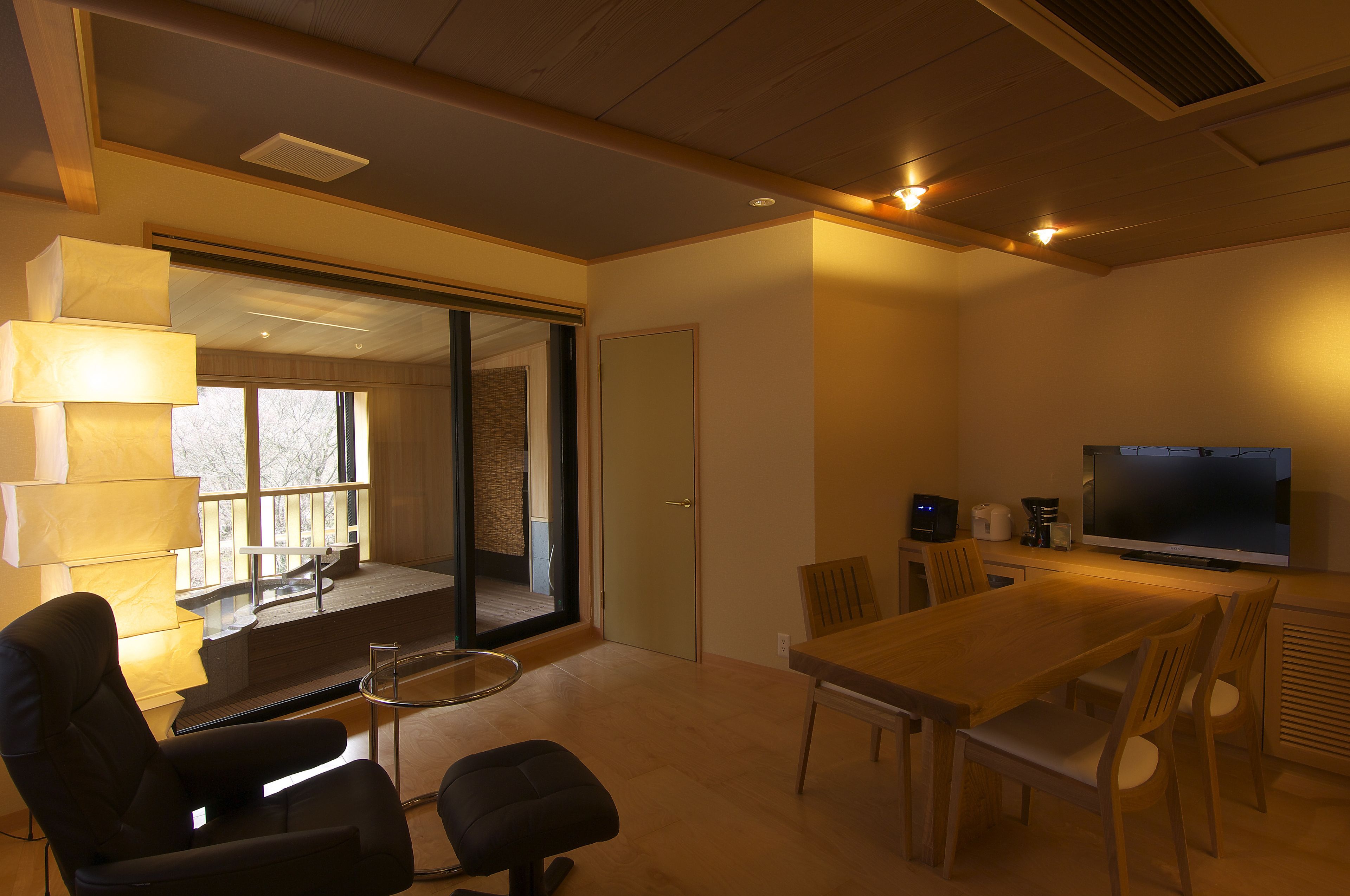 Una sala de estar moderna con una mesa de comedor de madera, sillas, un sofá y un televisor.