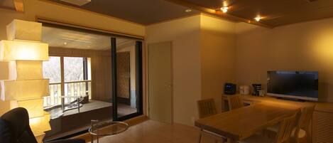 A modern living room with a wooden dining table, chairs, a sofa, and a TV.