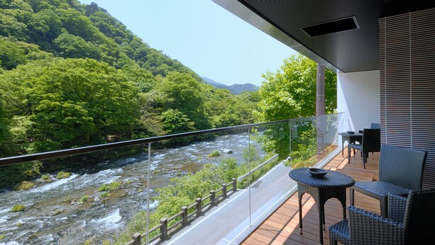 A balcony with a view of a river and forested hills.