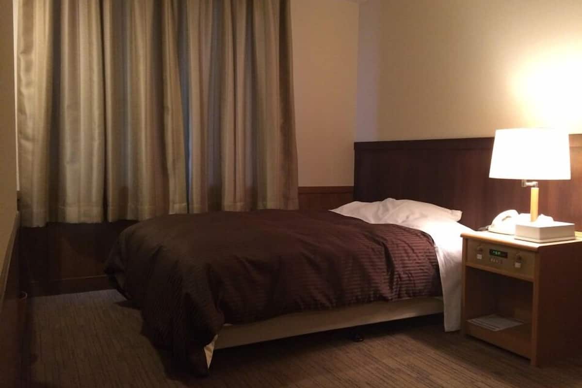 A hotel room with a bed, a nightstand with a lamp, a telephone, and a wall clock.