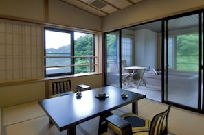 A traditional Japanese room with tatami flooring, a low table with tea sets, and a sliding glass door leading to a balcony with a view of greenery.