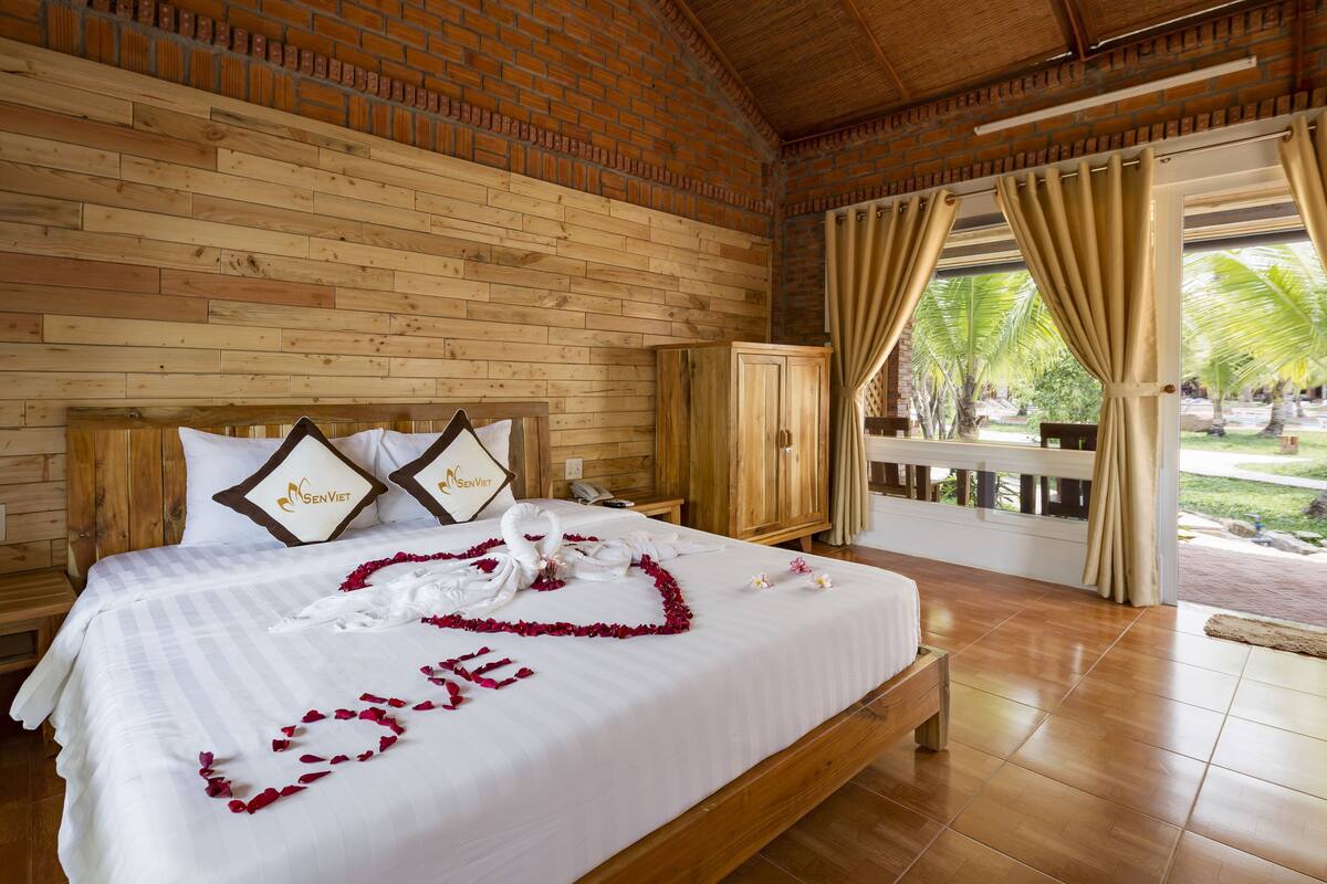 Een hotelkamer met een houten hoofdeinde, een bed met een witte sprei en een rozenblaadjesarrangement in de vorm van het woord 'LOVE'.