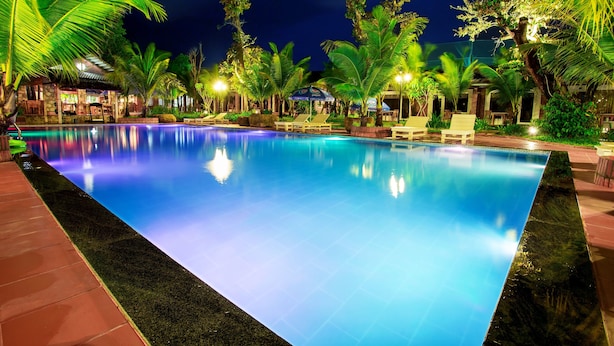 A nighttime swimming pool with palm trees and lounge chairs, surrounded by well-lit buildings. - Sen Viet Phu Quoc Resort Sport & Spa (Phu Quoc)