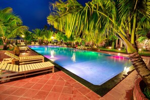 A nighttime swimming pool with lounge chairs and palm trees.