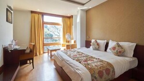 A hotel room with a large bed, a desk with a chair, a window with curtains, and a view of trees outside. - The Golden Crest (Gangtok)