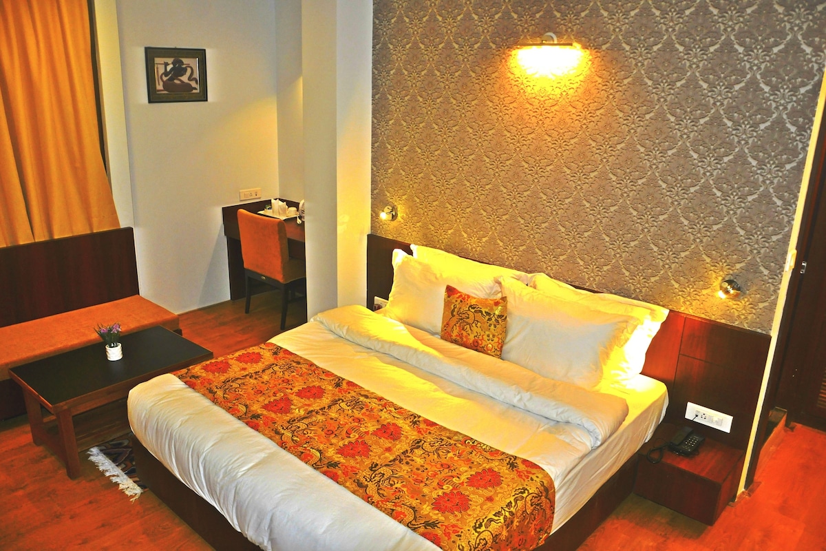 A hotel room with a bed, bedside table, chair, and a wall-mounted light fixture.
