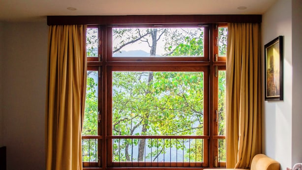 A room with a large window, a table with a plant, a chair, and a small table with a cup. - The Golden Crest (Gangtok)