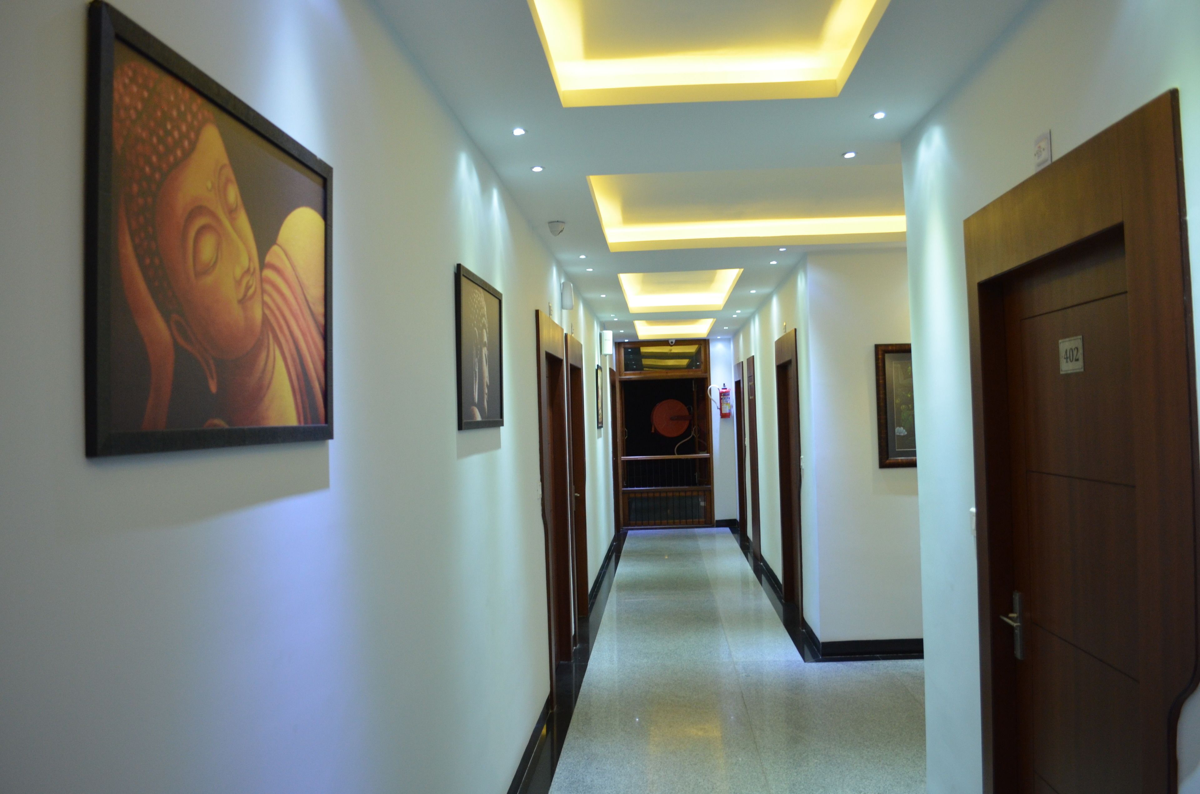 A hotel corridor with framed artwork on the walls, a wooden door on the right, and a ceiling with recessed lighting.
